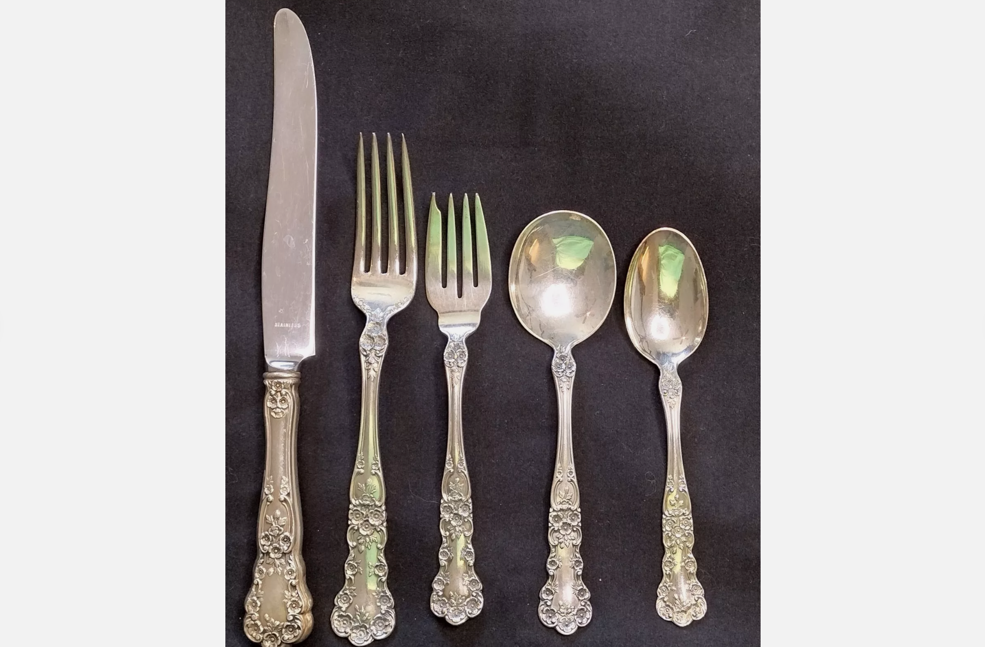 Set of five antique silverware pieces with ornate floral handles, displayed on a dark background