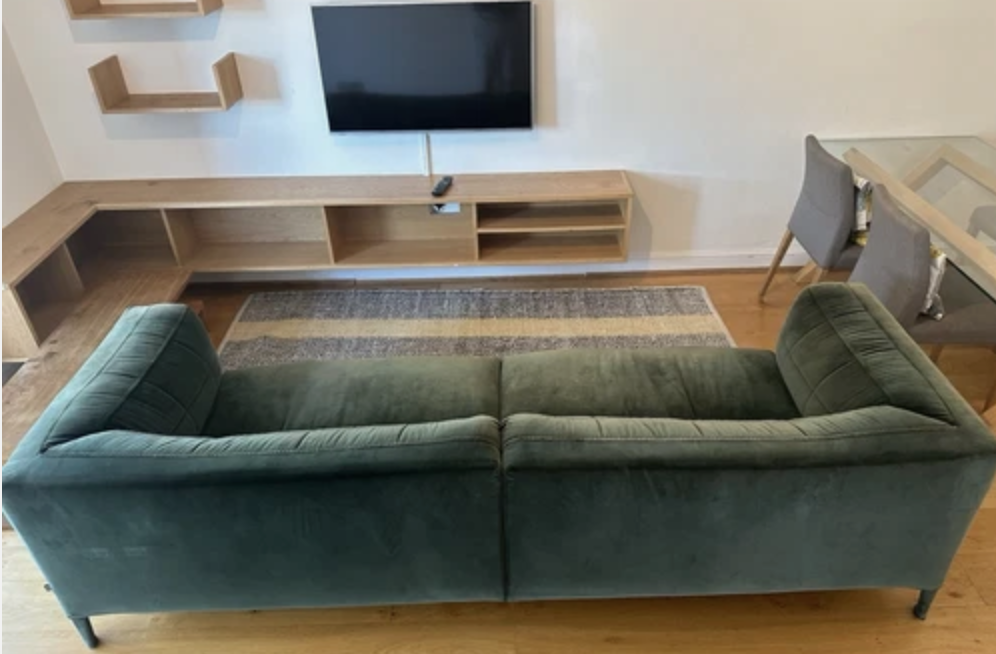 Green velvet B&B Italia sofa with a low backrest and clean lines, positioned in a modern living room facing a mounted TV and wooden media console