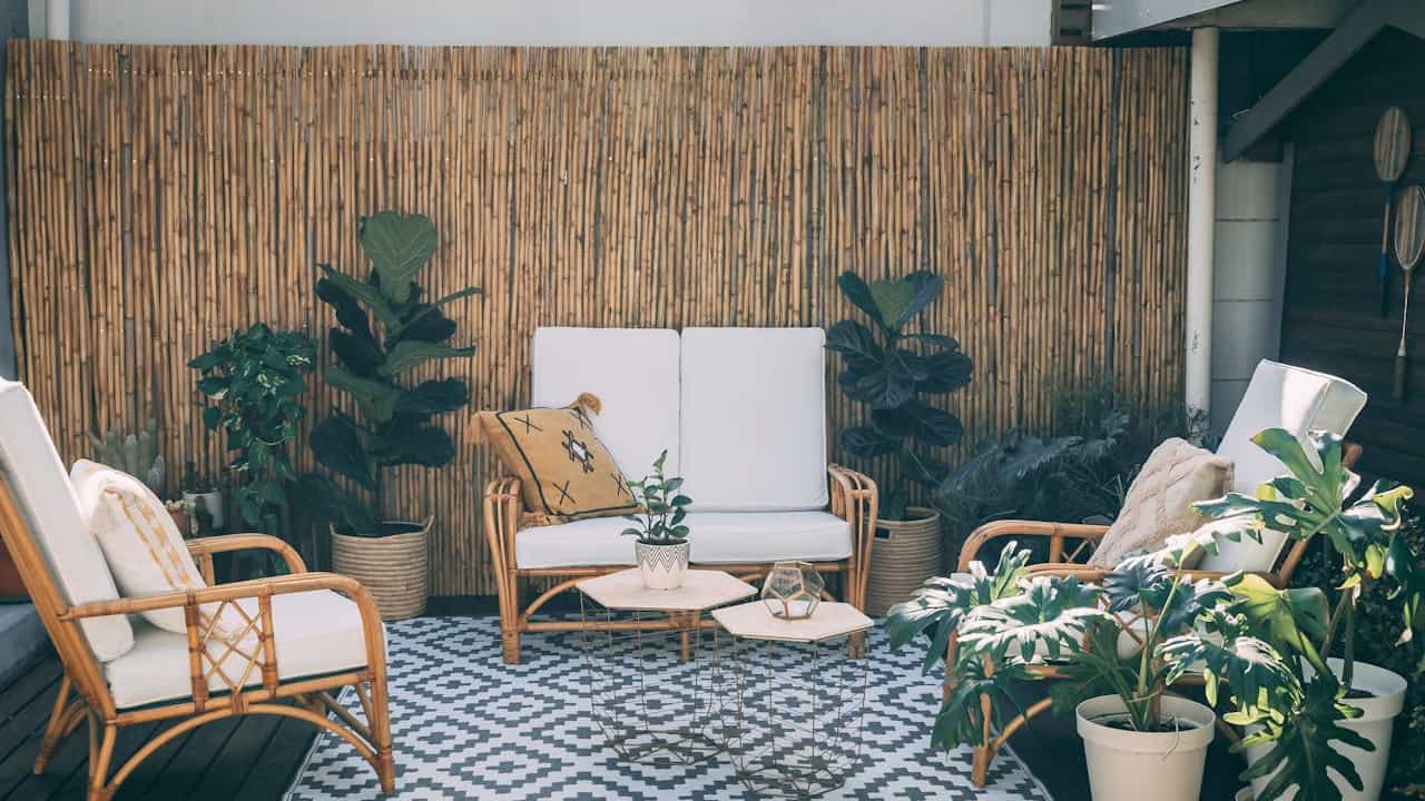 Outdoor seating area with bamboo room dividers, rattan furniture with white cushions, potted plants, and a geometric-patterned rug