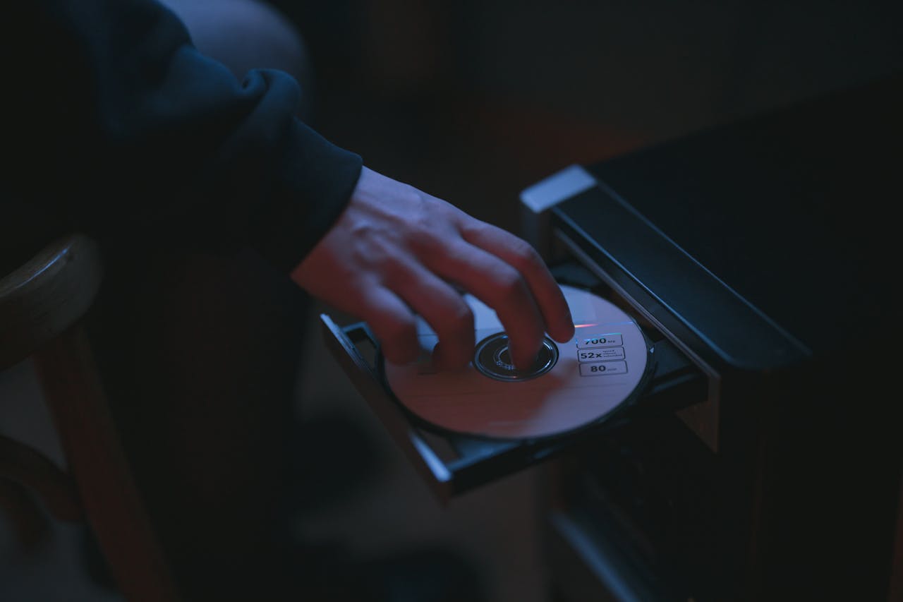 Hand inserting a CD into a CD player tray, dimly lit room, dark atmosphere, close-up view of disc labeled 700MB