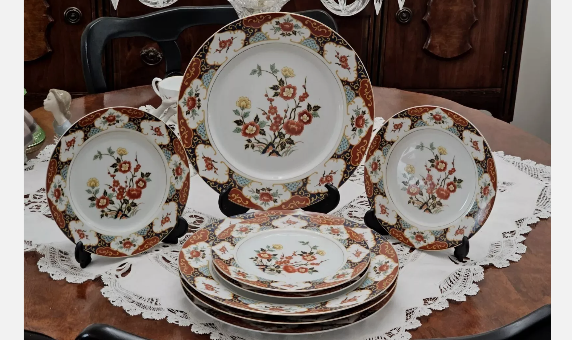 Complete vintage china dinnerware set with floral and gold detailing, displayed on a lace-covered wooden table