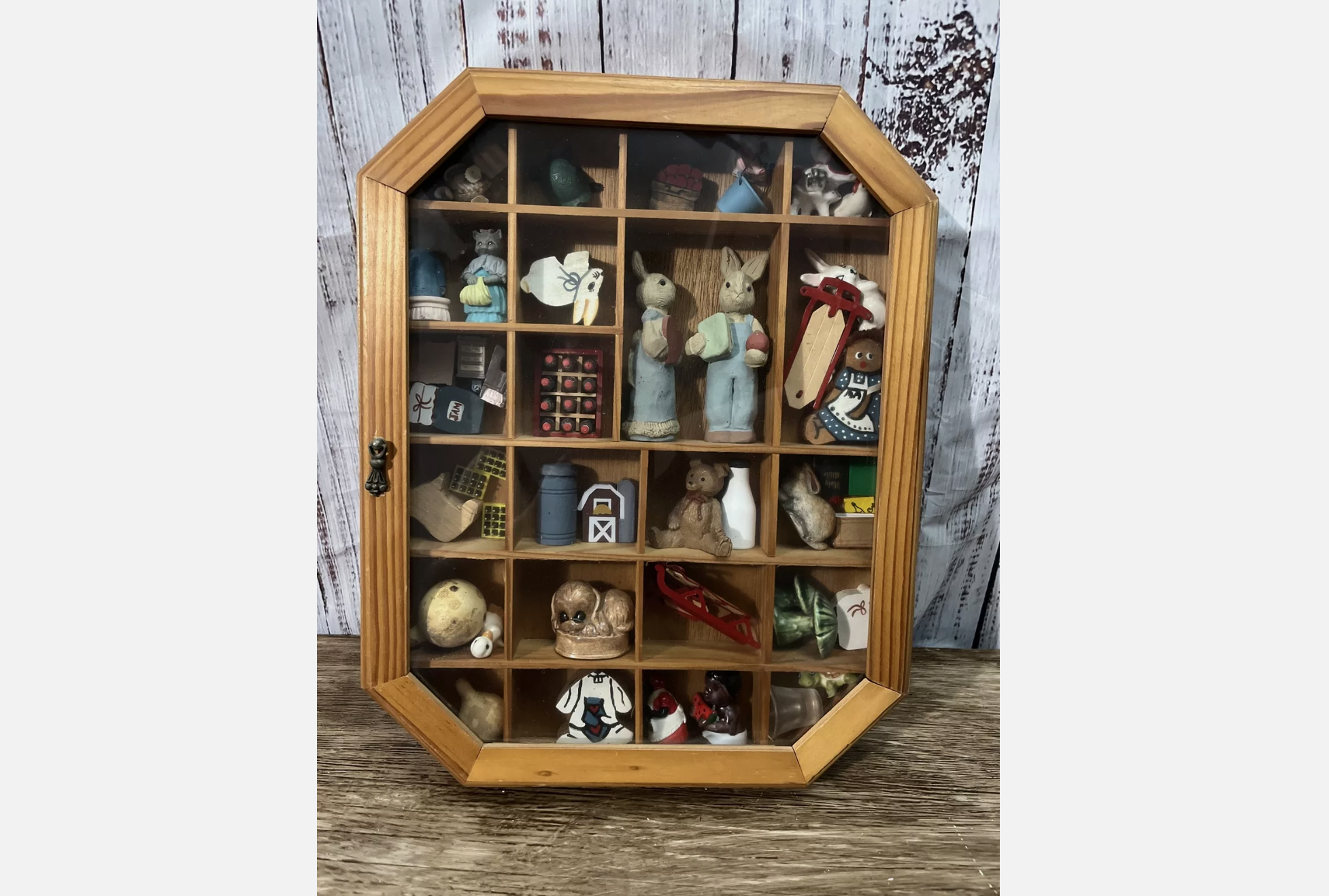 Wooden octagon-shaped curio cabinet with glass front, filled with miniature collectible figurines including animals, toys, and seasonal items
