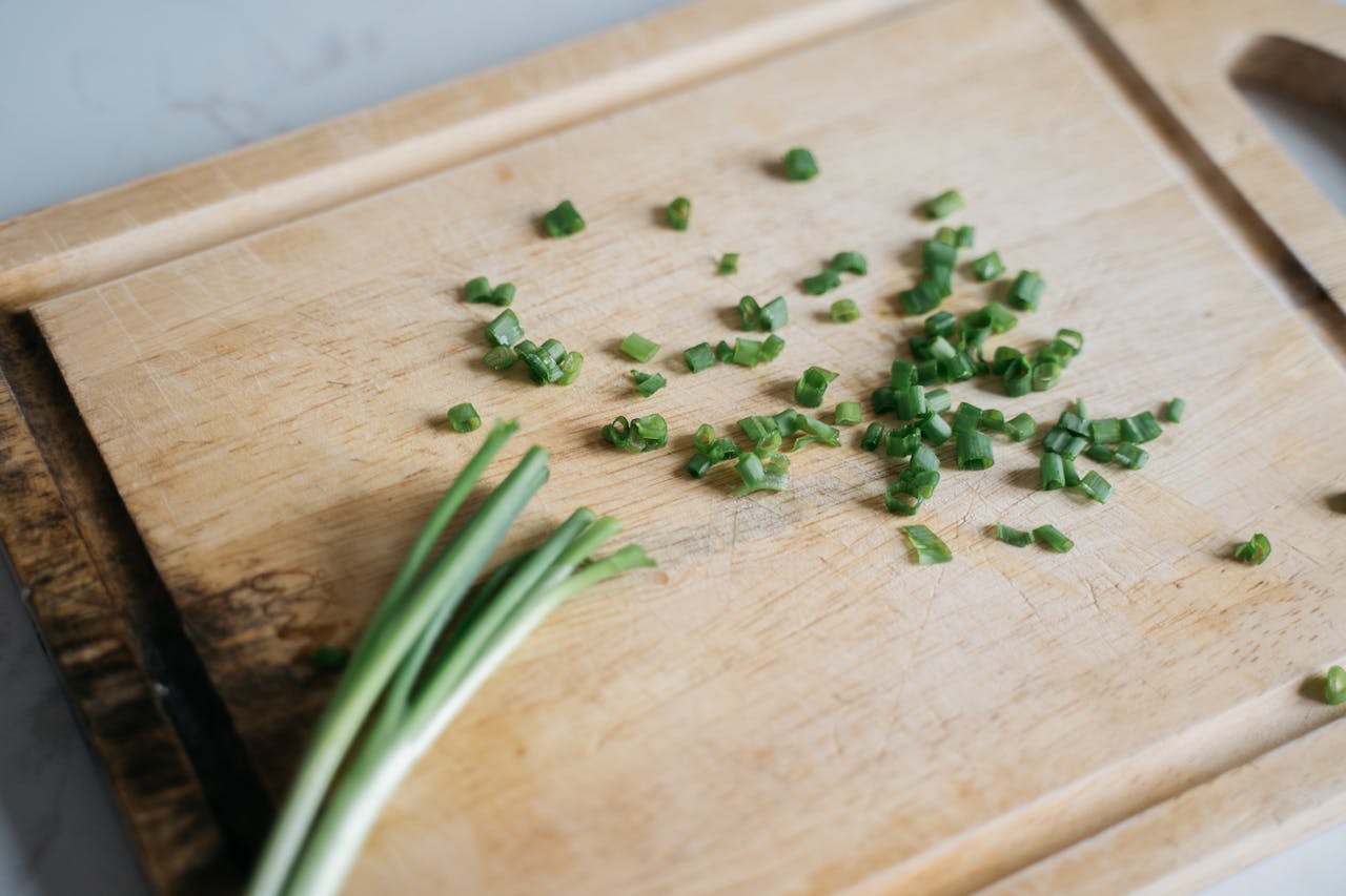 Chopped green onions on a wooden cutting board with whole stalks on the side, set on a light kitchen countertop