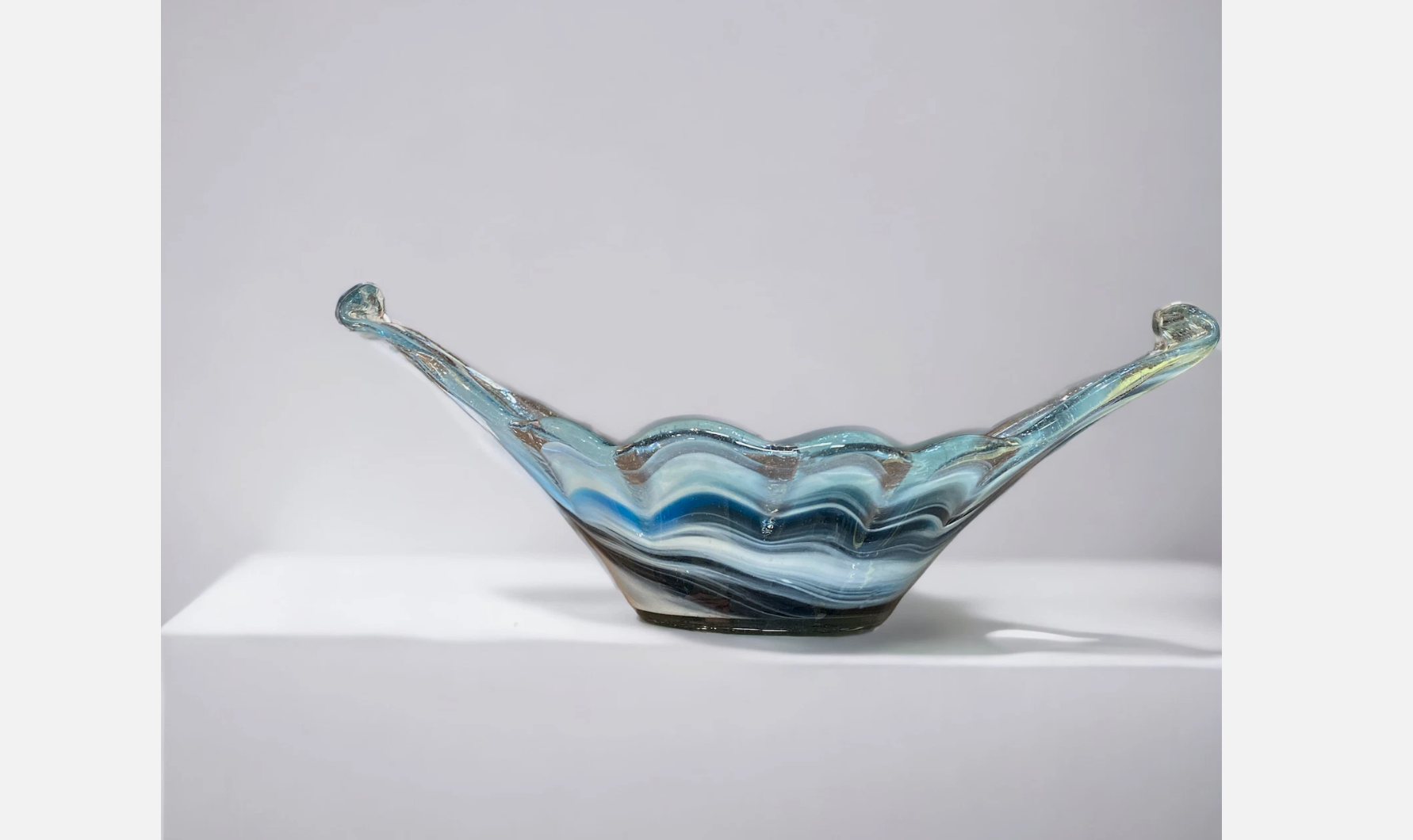 Blue and white swirled glass centerpiece bowl with curled ends and a wavy rim, displayed on a white surface