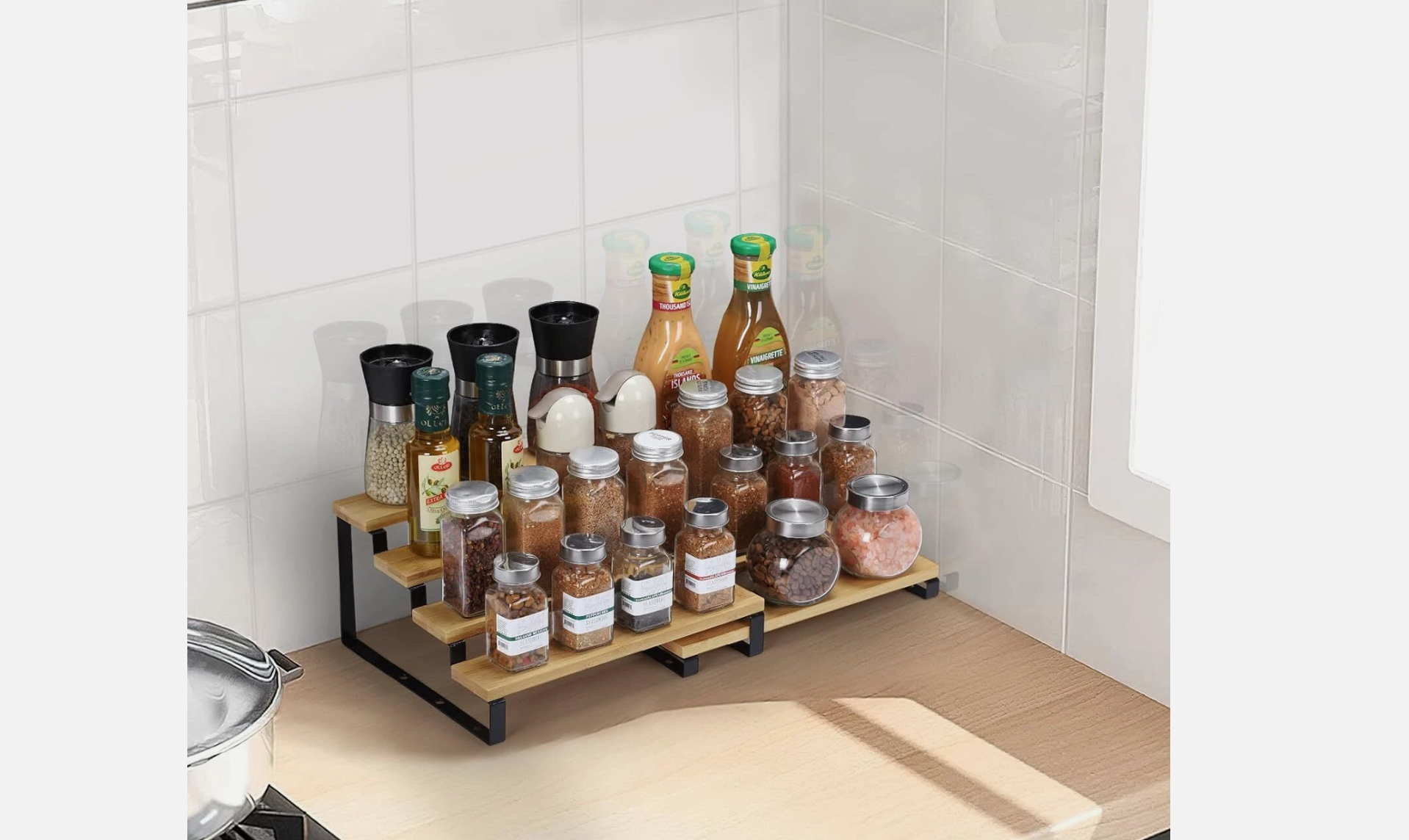 Expandable spice rack on kitchen countertop, neatly organized with various glass jars of spices, salt, oil bottles, and salad dressings