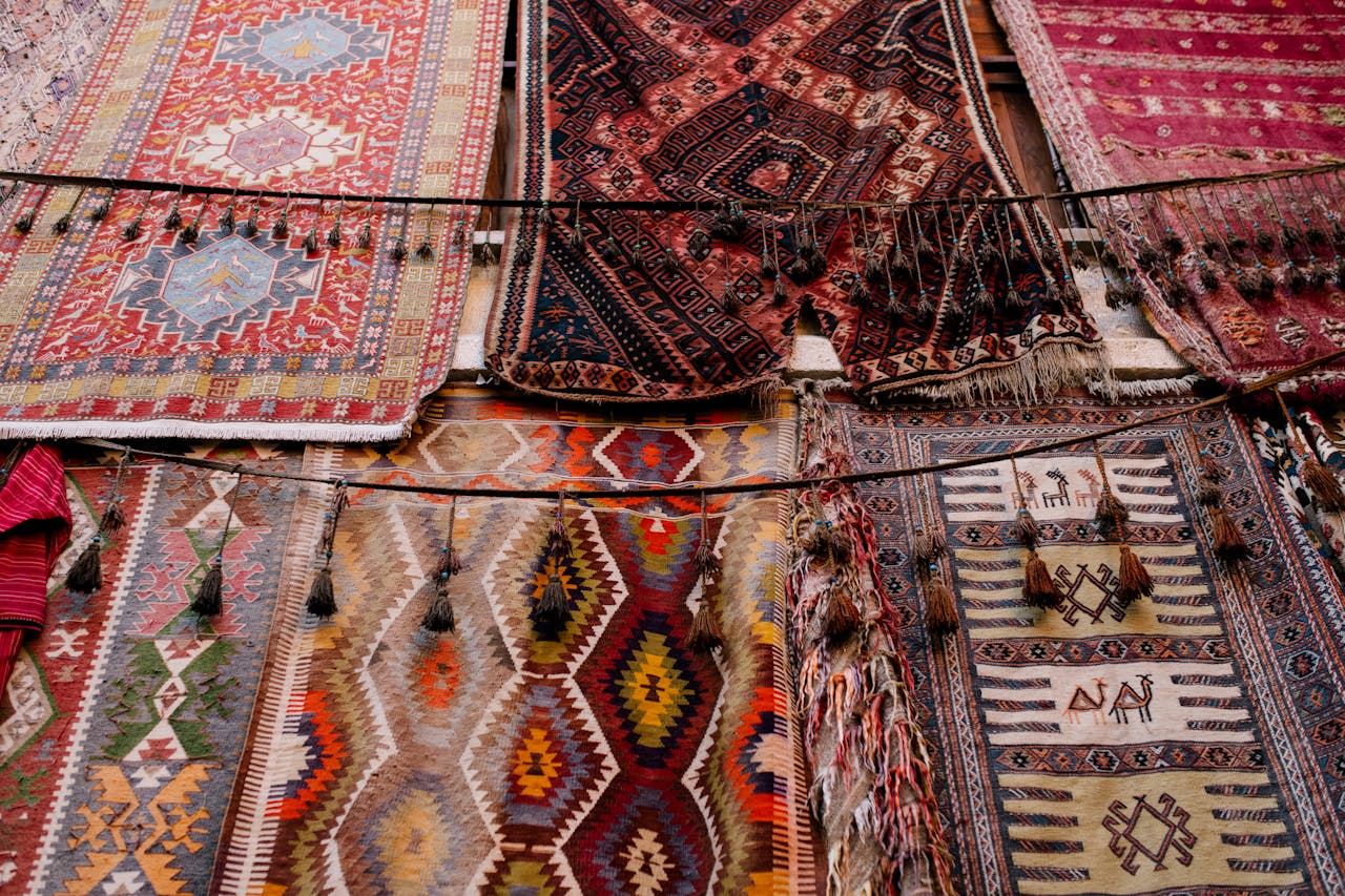 Colorful handwoven rugs with intricate patterns and tassels hanging in rows at a market stall