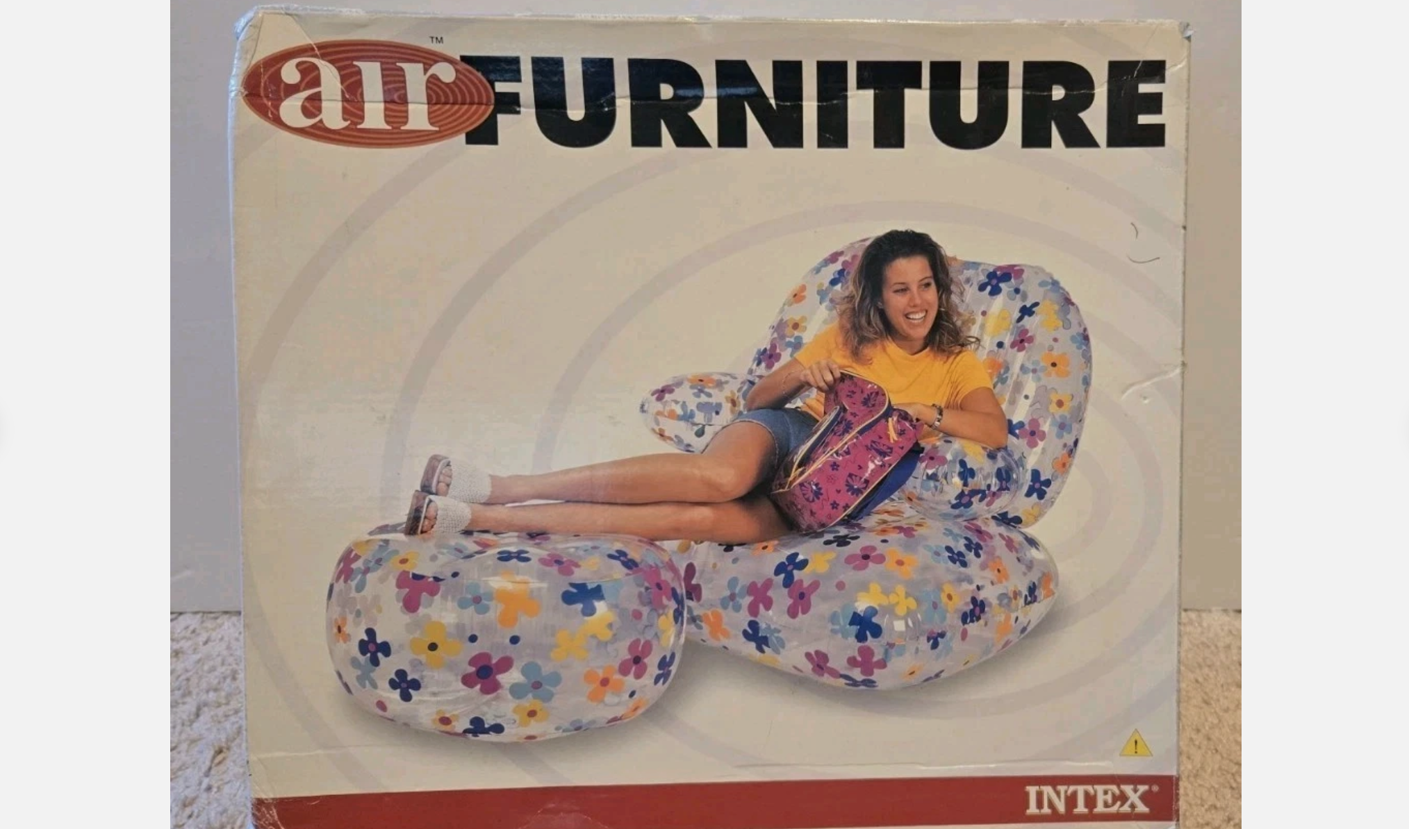 Box displaying inflatable plastic chair and ottoman with colorful flower print, featuring a smiling girl lounging