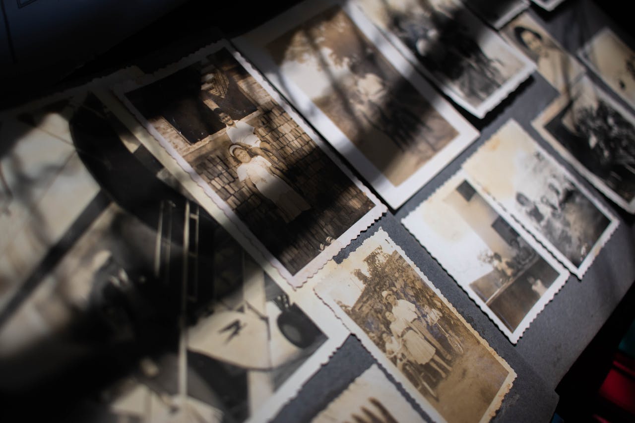 Scattered vintage black and white family photographs on a dark surface, partially shadowed by light and objects