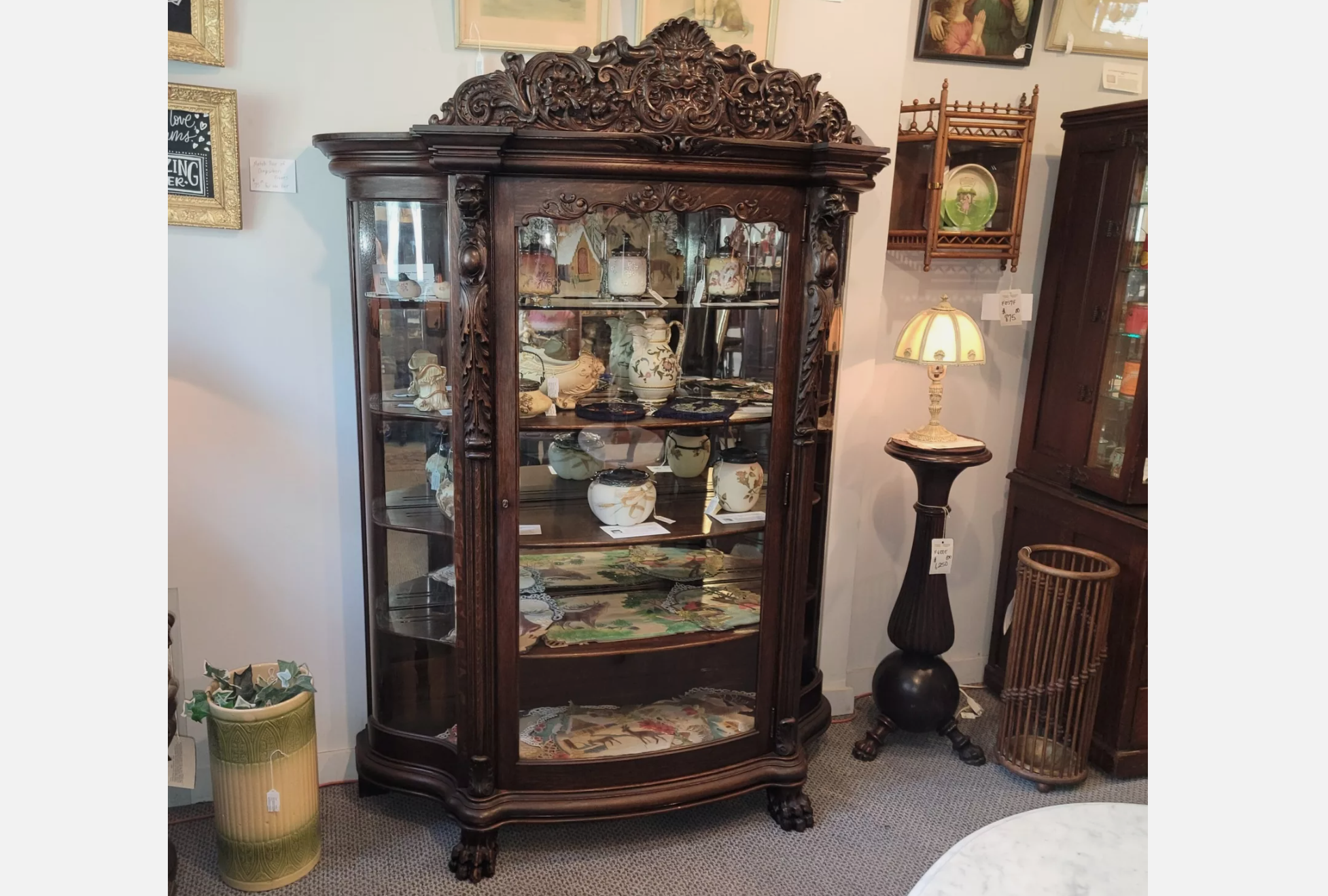 Dark wood ornate china cabinet with curved glass doors and carved detailing, filled with antique ceramic and porcelain collectibles