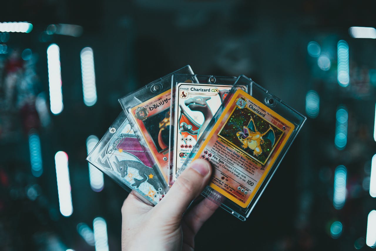 Hand holding five rare Charizard Pokémon cards in protective plastic sleeves, dimly lit background with glowing blue lights