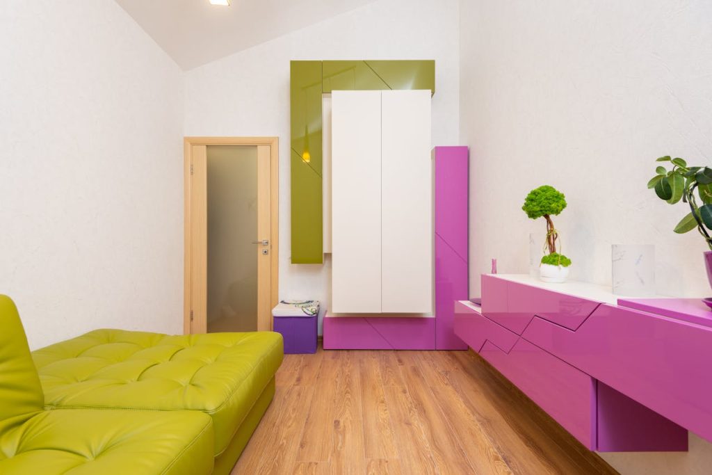 Modern living room with lime green sofa, glossy pink and white storage units, green accent cabinet, potted bonsai tree, light wood flooring