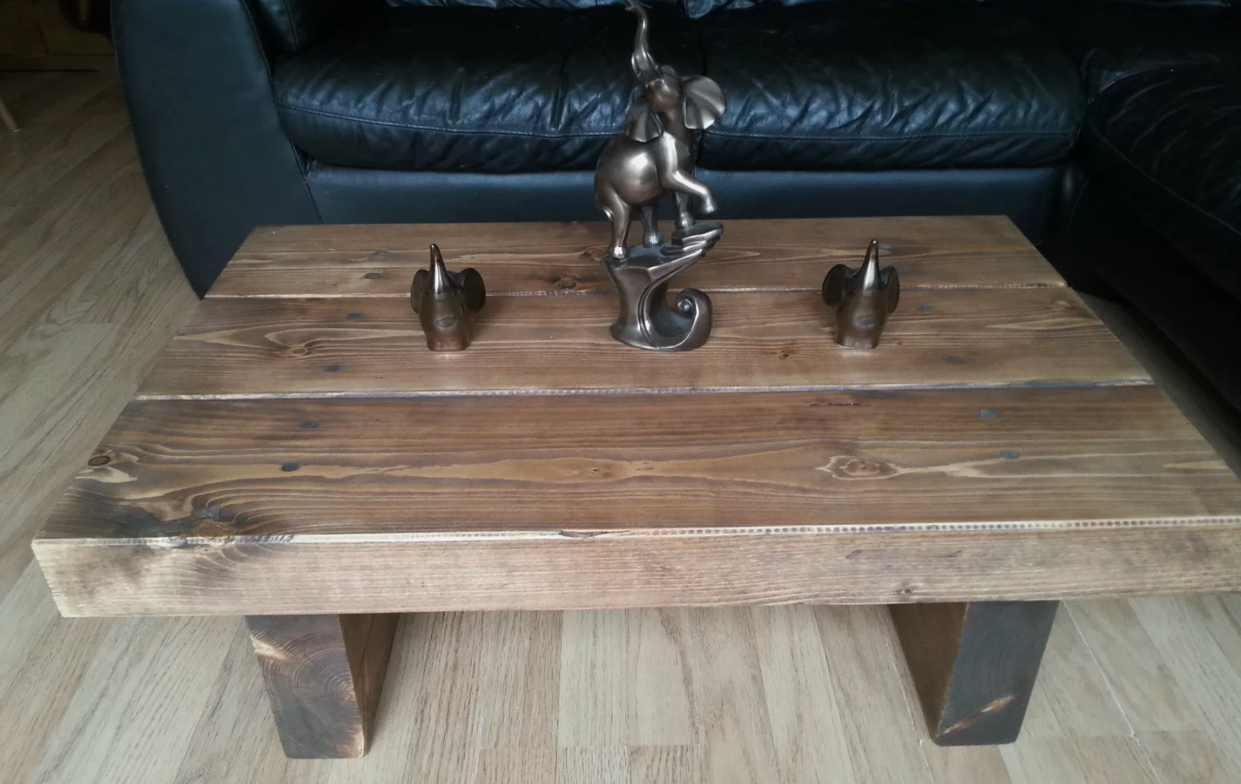 Reclaimed wood coffee table with dark metal elephant figurines, placed in front of a black leather couch on light wood flooring