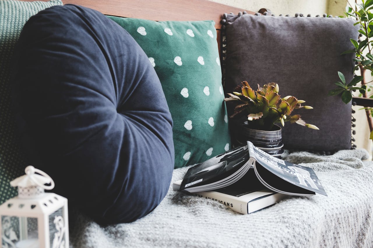 Round navy blue pintuck pillow, green pillow with white dots, gray pompom pillow, plant in striped pot, books on gray knit throw