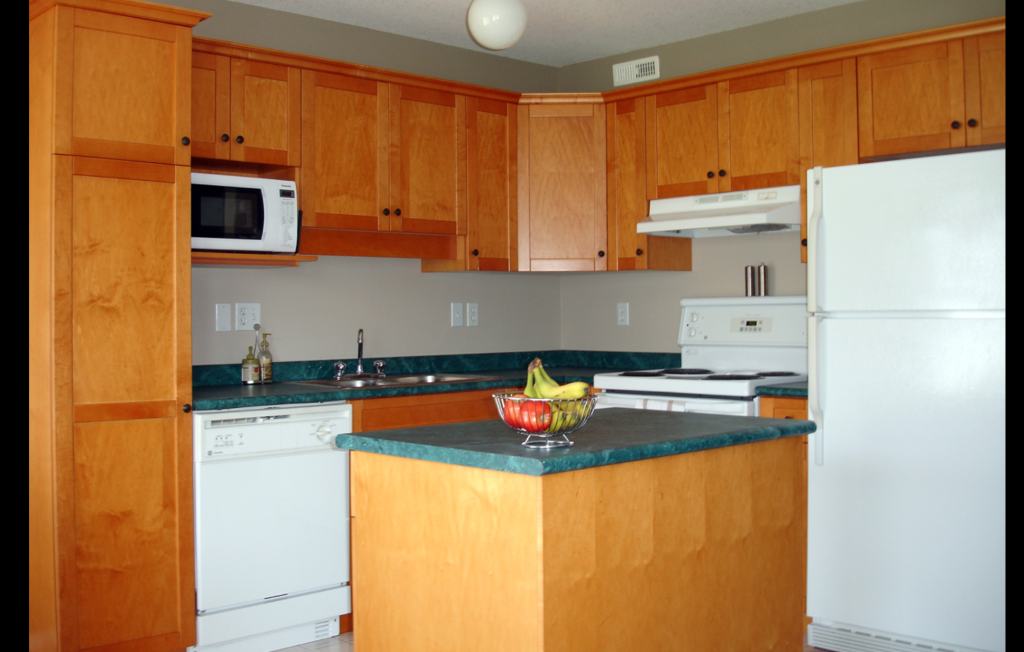 Kitchen with honey-toned shaker-style cabinets and green countertops, echoing the double-drenched, retro-leaning green cabinetry look of Valspar's Warm Eucalyptus palette
