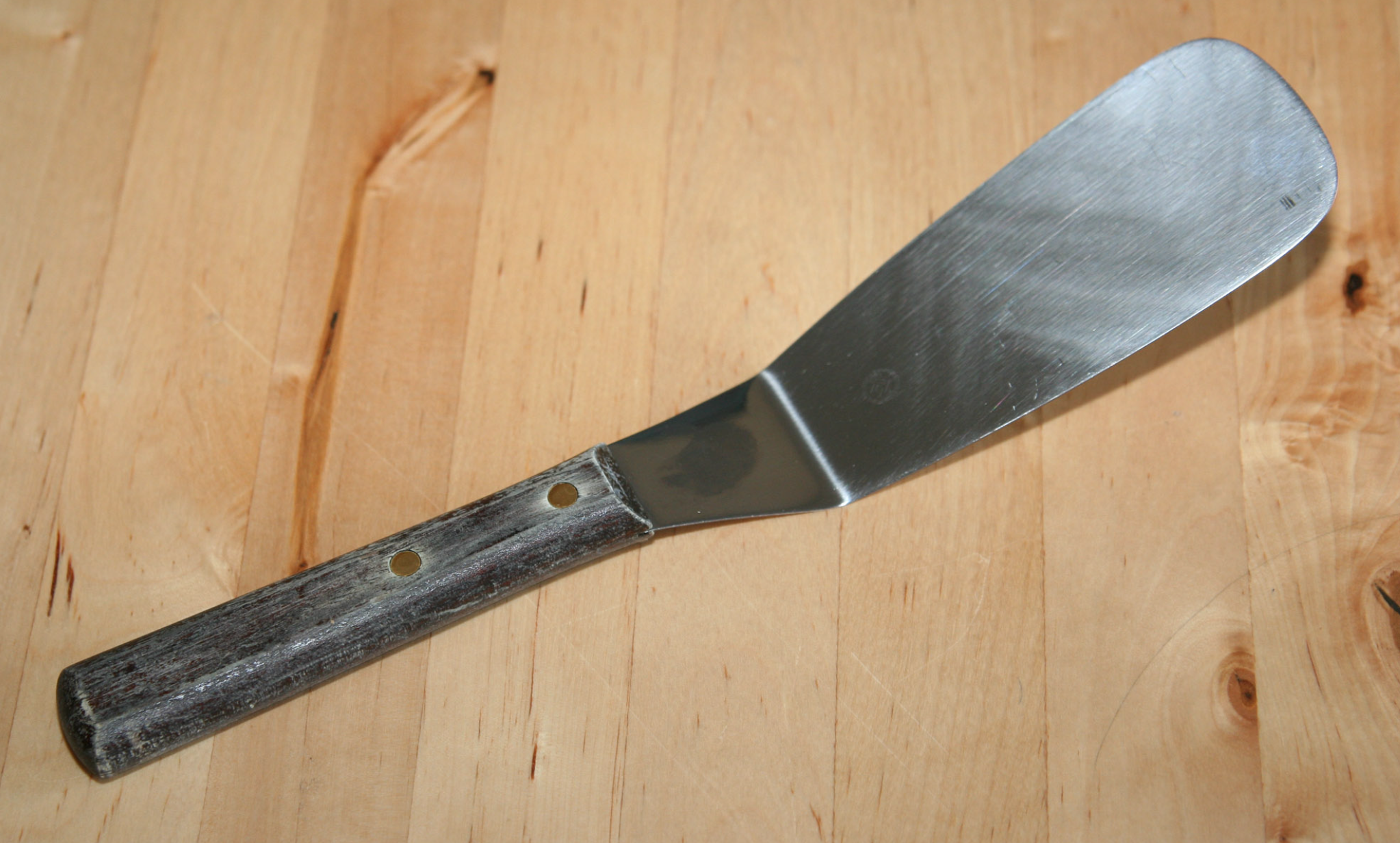 Stainless steel spatula with a worn wooden handle resting on a light wood countertop