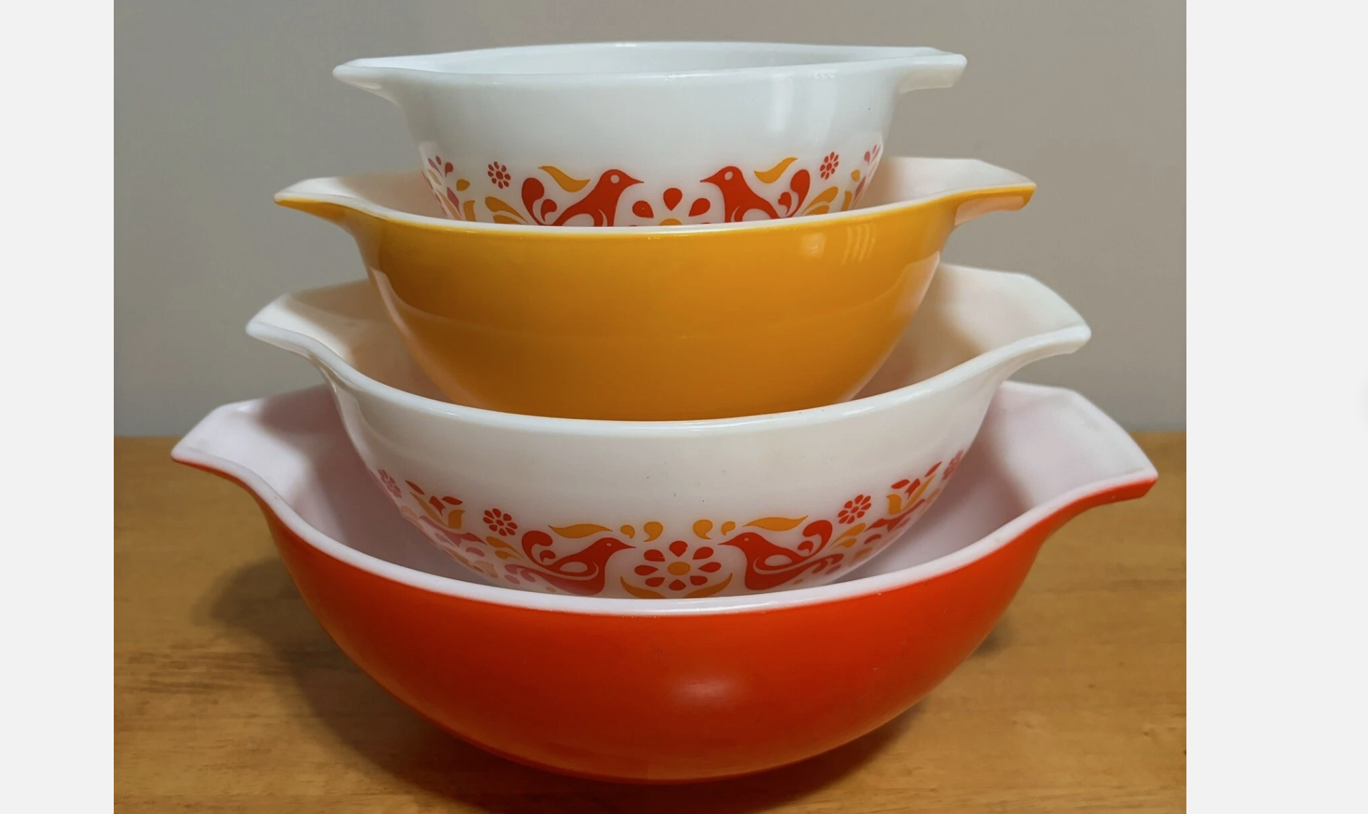 Stack of vintage Pyrex mixing bowls in orange, yellow, and white with red bird and floral motif