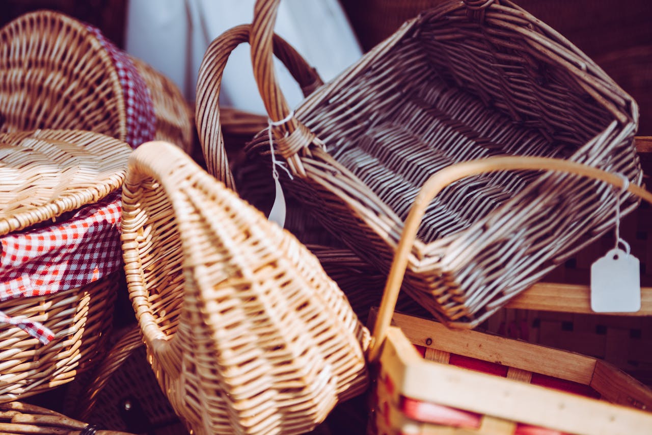 Assorted wicker baskets with handles, some with gingham fabric liners and price tags, arranged closely together in warm sunlight