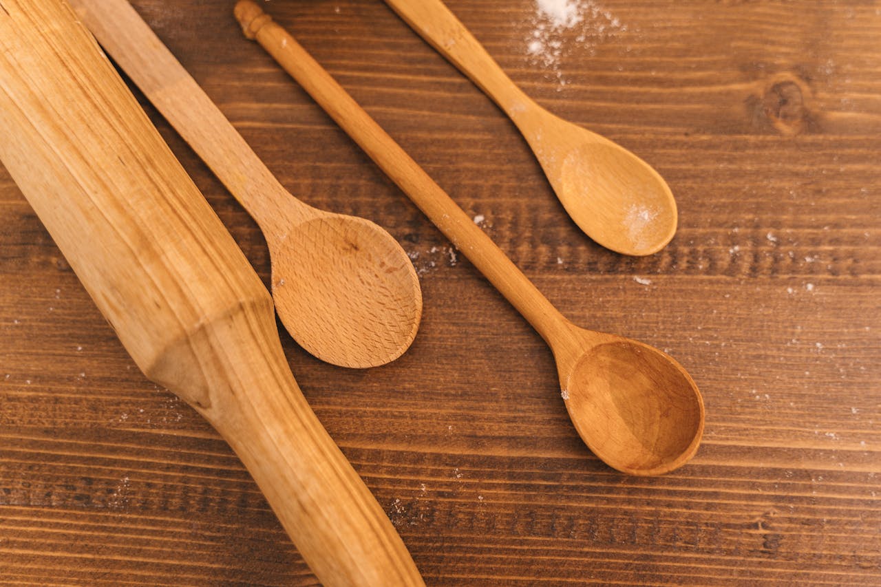 Wooden spoons and rolling pin on a dark wooden surface, lightly dusted with flour, arranged in a rustic kitchen setting