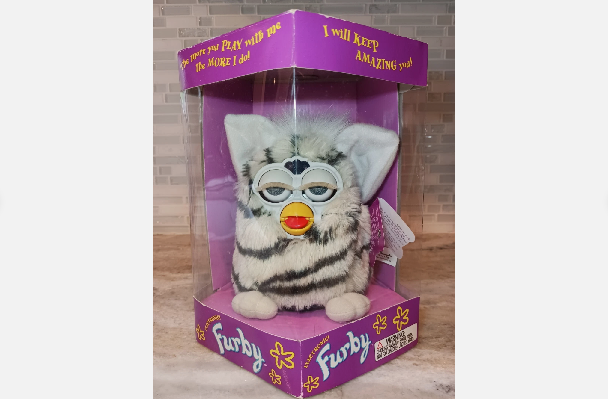1998 black and white striped Furby toy in original purple packaging with plastic window, displayed upright on a marble countertop
