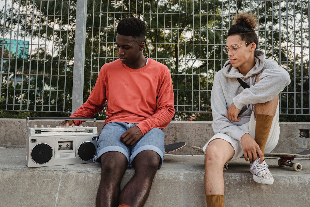 two friends hanging out at a skatepark, listening to music from a retro boombox, discussing skate tricks, relaxing after skateboarding