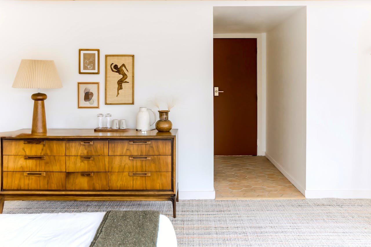 Mid-century modern wooden sideboard with nine drawers, topped with a ceramic jug, two glasses, and a sculptural table lamp