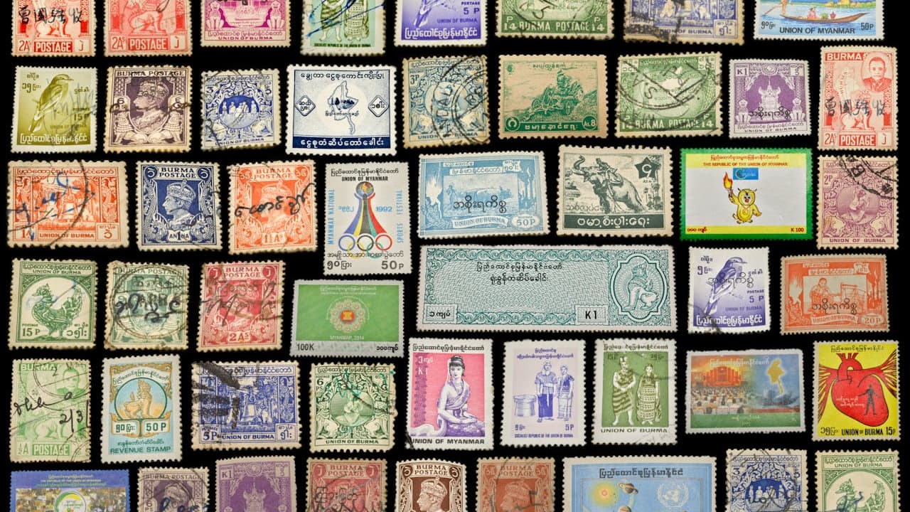 Colorful vintage postage stamps, arranged in a grid pattern, various countries and designs, different sizes and colors, displayed on a black background, used for collection or display purposes
