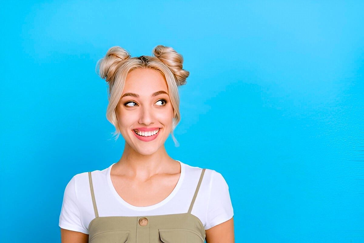 Photo of optimistic blond buns hairdo lady look empty space wear t-shirt overall isolated on blue color background