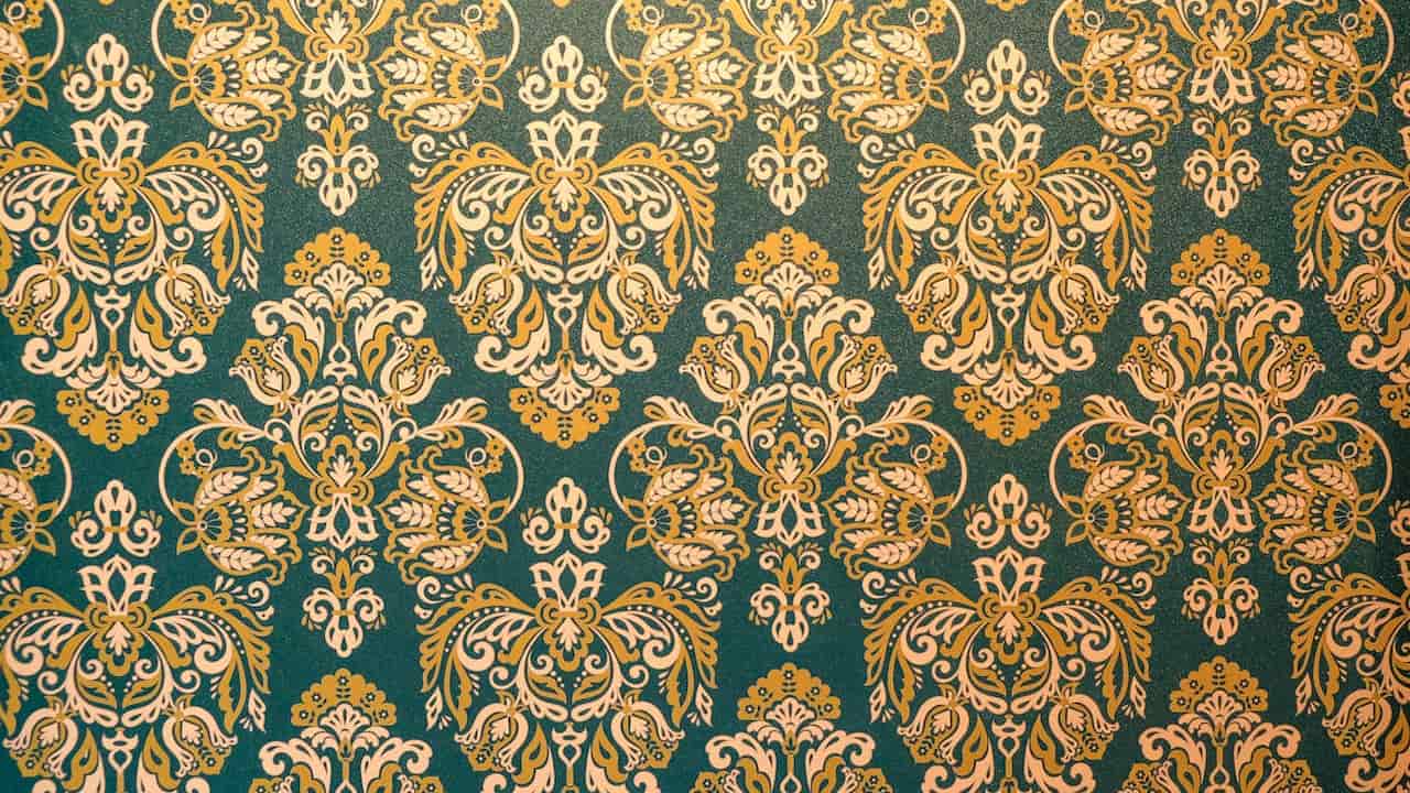 A richly detailed vintage wallpaper with an ornate damask pattern in gold and cream over a deep teal background, repeating symmetrically across the surface