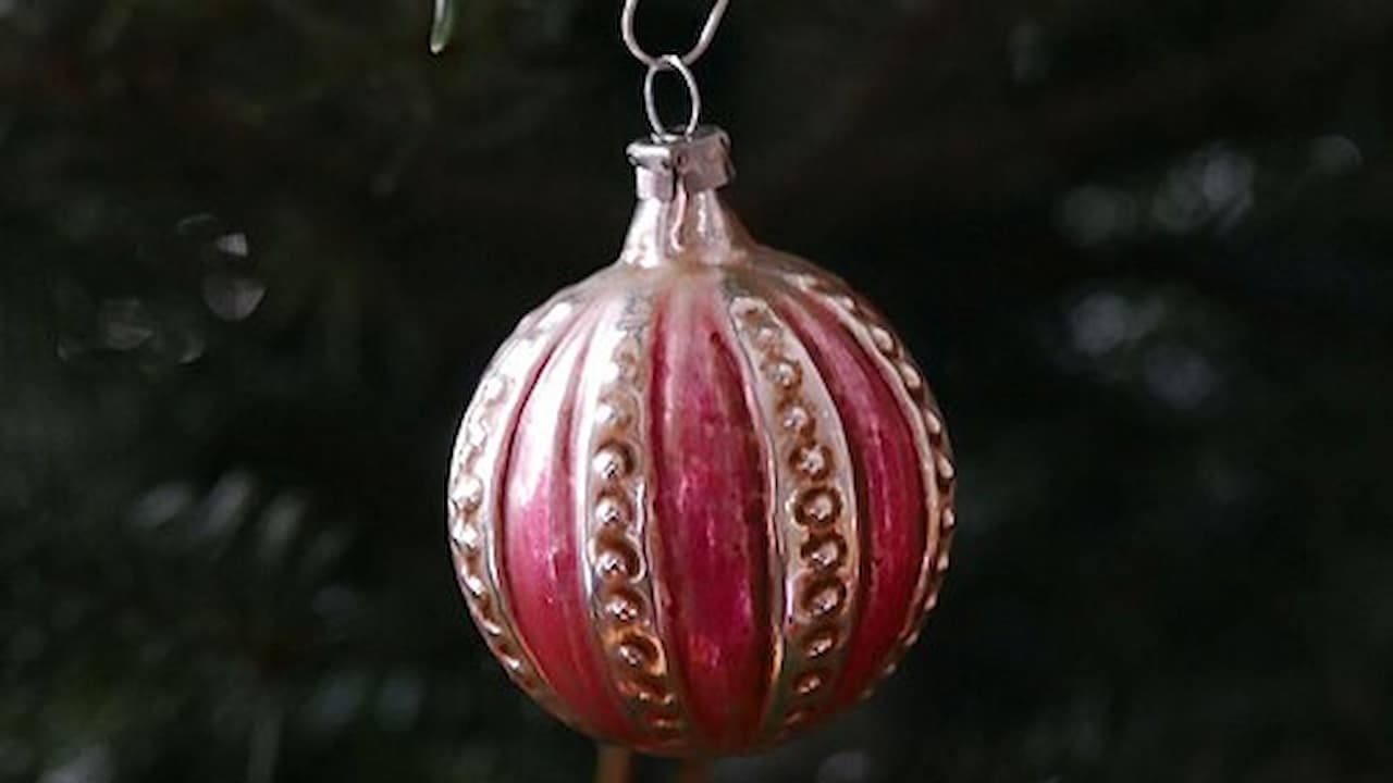 Red and gold Christmas ornament, round shape, glittery gold patterns, hanging from a tree branch, dark green pine needles in background