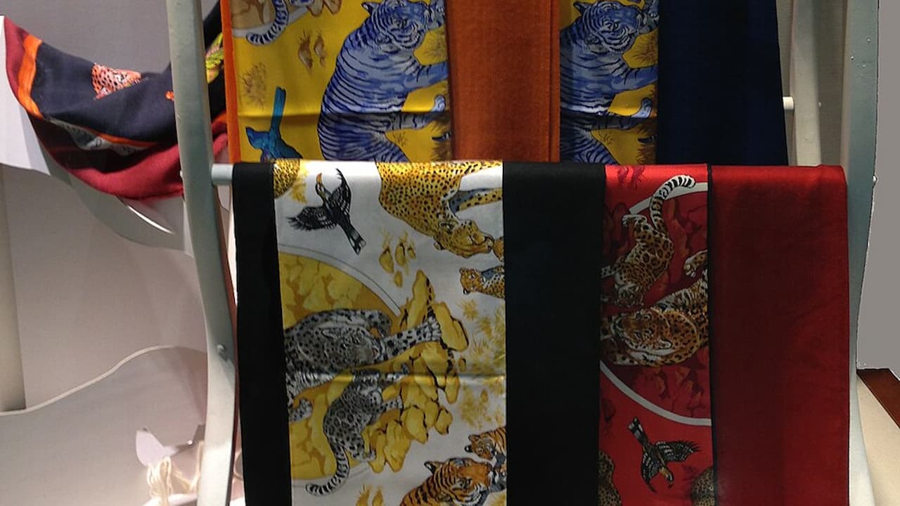 Colorful patterned fabrics hanging vertically, featuring vibrant hues like yellow, red, orange, and blue, with intricate floral and animal motifs, displayed on a rack in a store setting