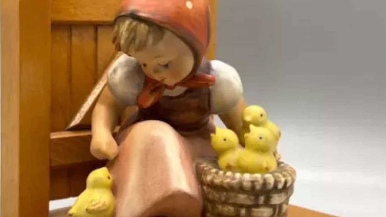 Ceramic figurine of a young girl in a red hood, sitting on a bench, surrounded by yellow chicks, holding a basket full of chicks, light gray background, soft lighting