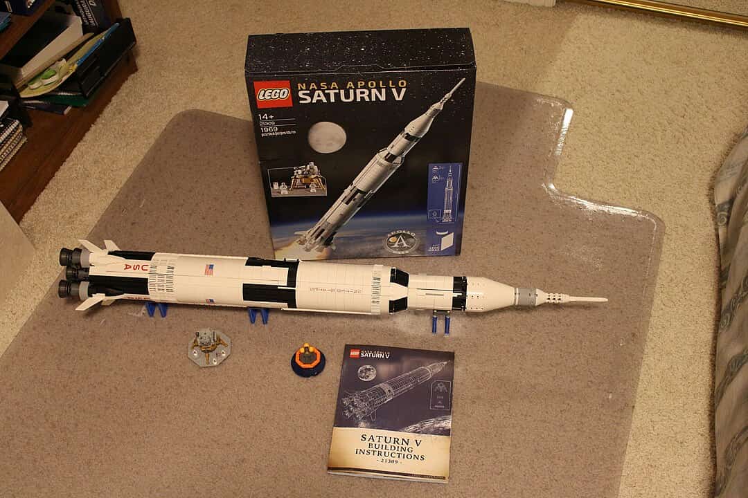 LEGO NASA Apollo Saturn V rocket model assembled and displayed on carpet, with instruction manual and box set showing set number 21309