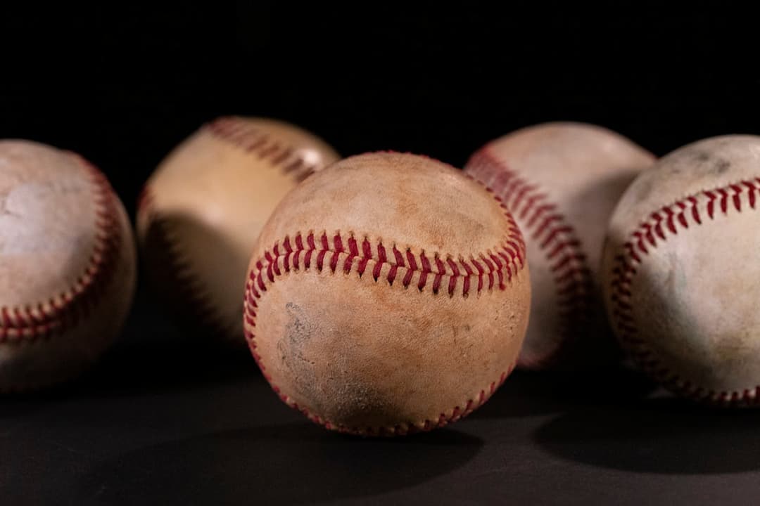 Close-up of five worn baseballs with red stitching, arranged on a dark surface against a black background