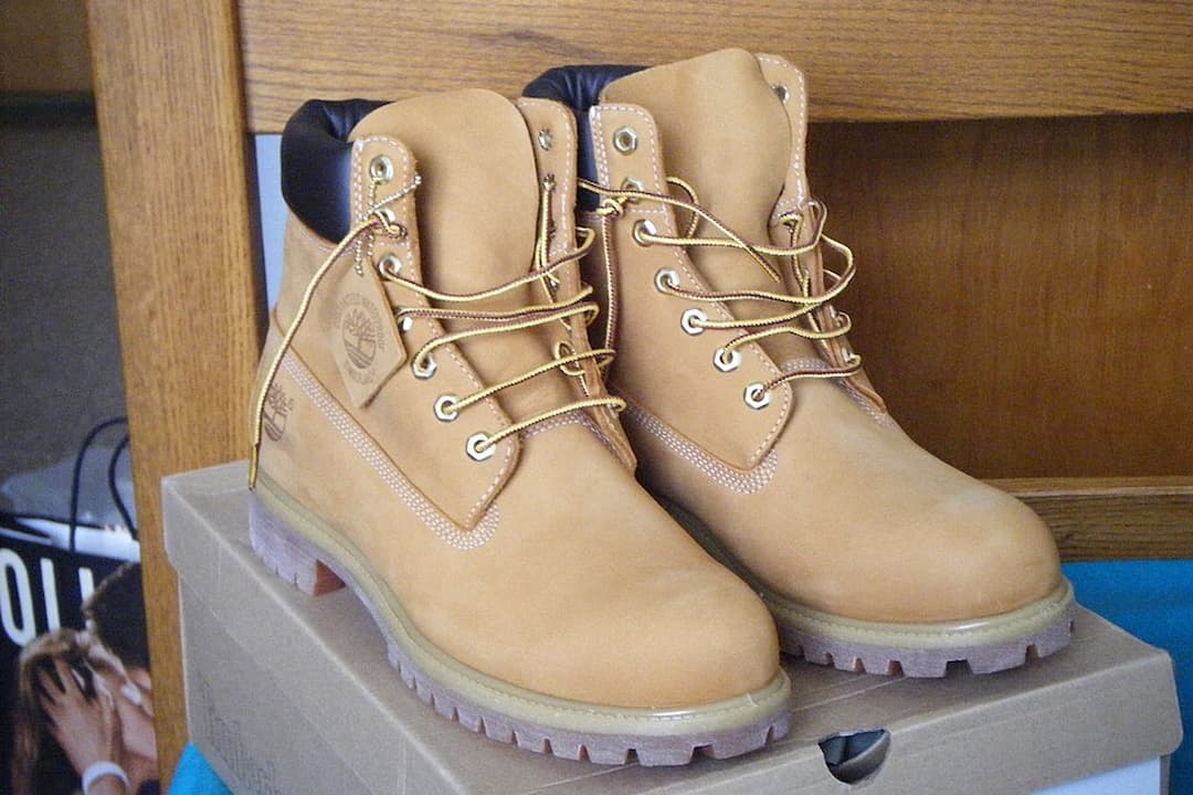 Pair of tan Timberland boots with padded black collars and yellow laces, placed on a cardboard shoebox indoors
