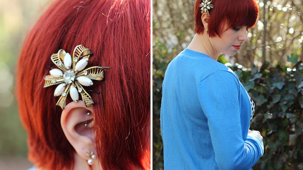 Close-up of a jeweled hair clip in red hair, person with short red hair wearing a blue top, outdoor natural background, sunlight highlighting hair accessory