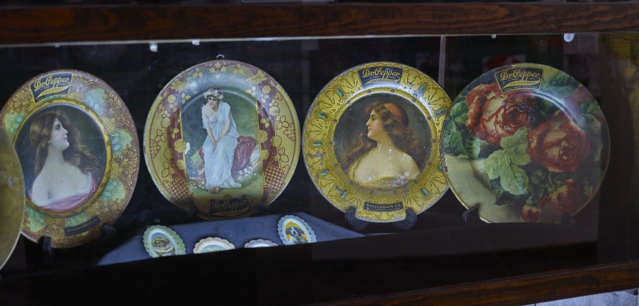 Decorative collector plates, four in a row, each featuring a portrait of a woman in vintage attire, ornate gold and floral borders, displayed in a dark wooden cabinet, reflective glass surface, classic and antique style