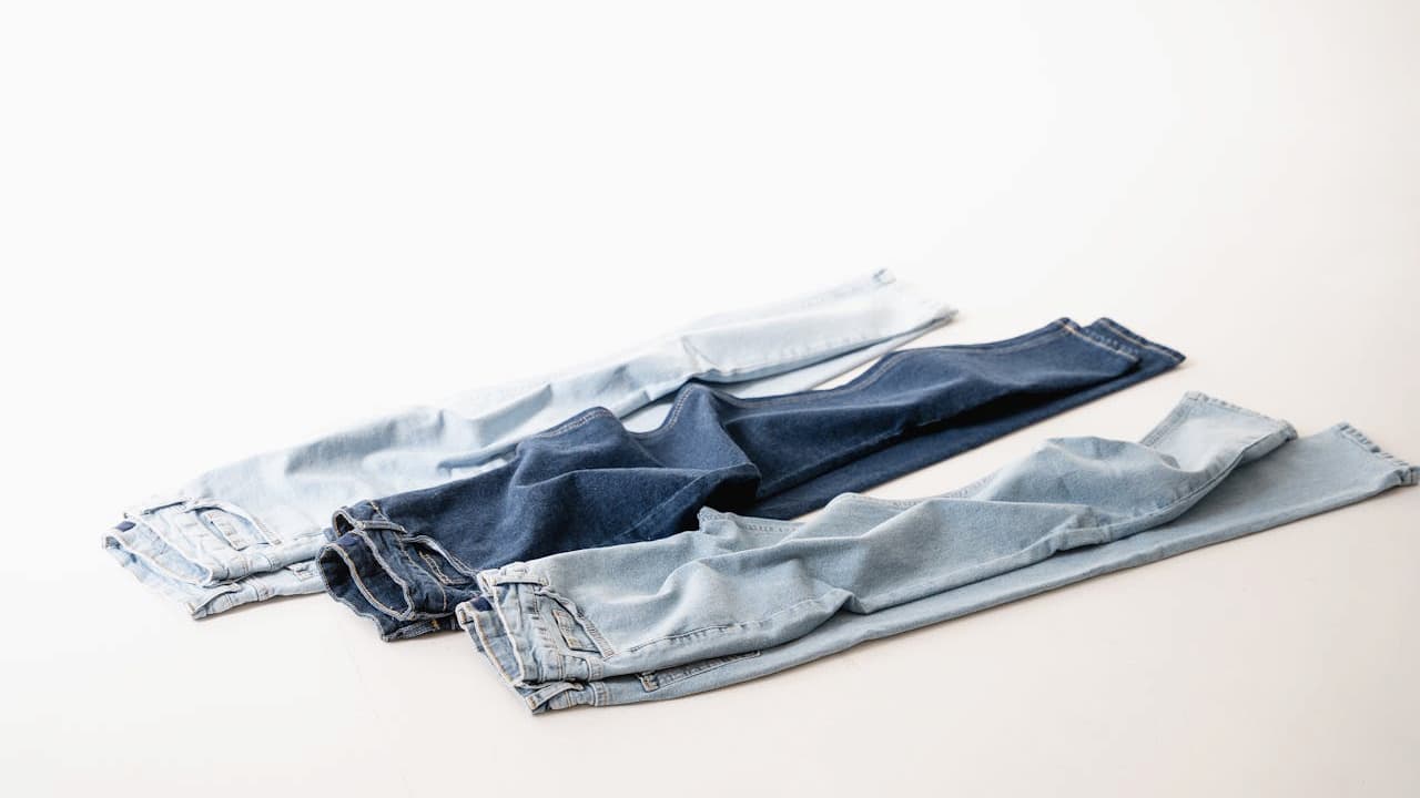 Three pairs of folded denim jeans, displayed on a white surface, in varying shades of blue, casual style, clean and neatly arranged