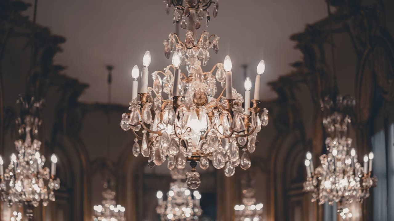 Elegant crystal chandeliers, ornate lighting fixtures, hanging in a grand hall, warm ambient glow, detailed gold accents, luxurious classical interior, high ceiling architecture, formal event or ball setting