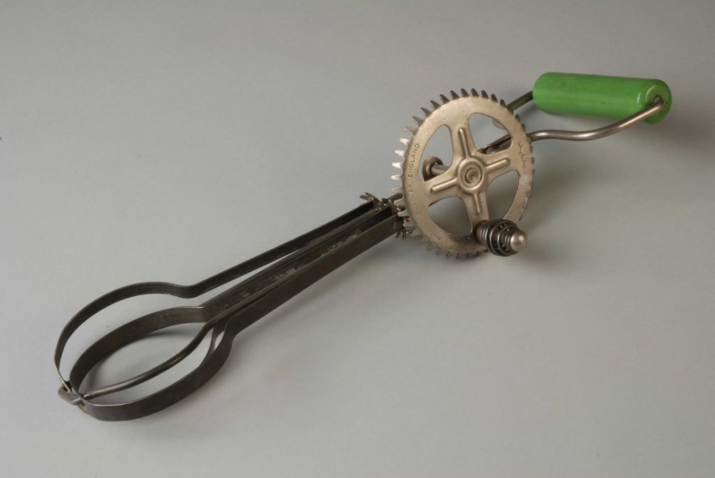 Handmixer met contraroterende bladen waarvan de aandrijving gemaakt is van gestanst blik met omgeslagen vertanding en met groen houten handgreep