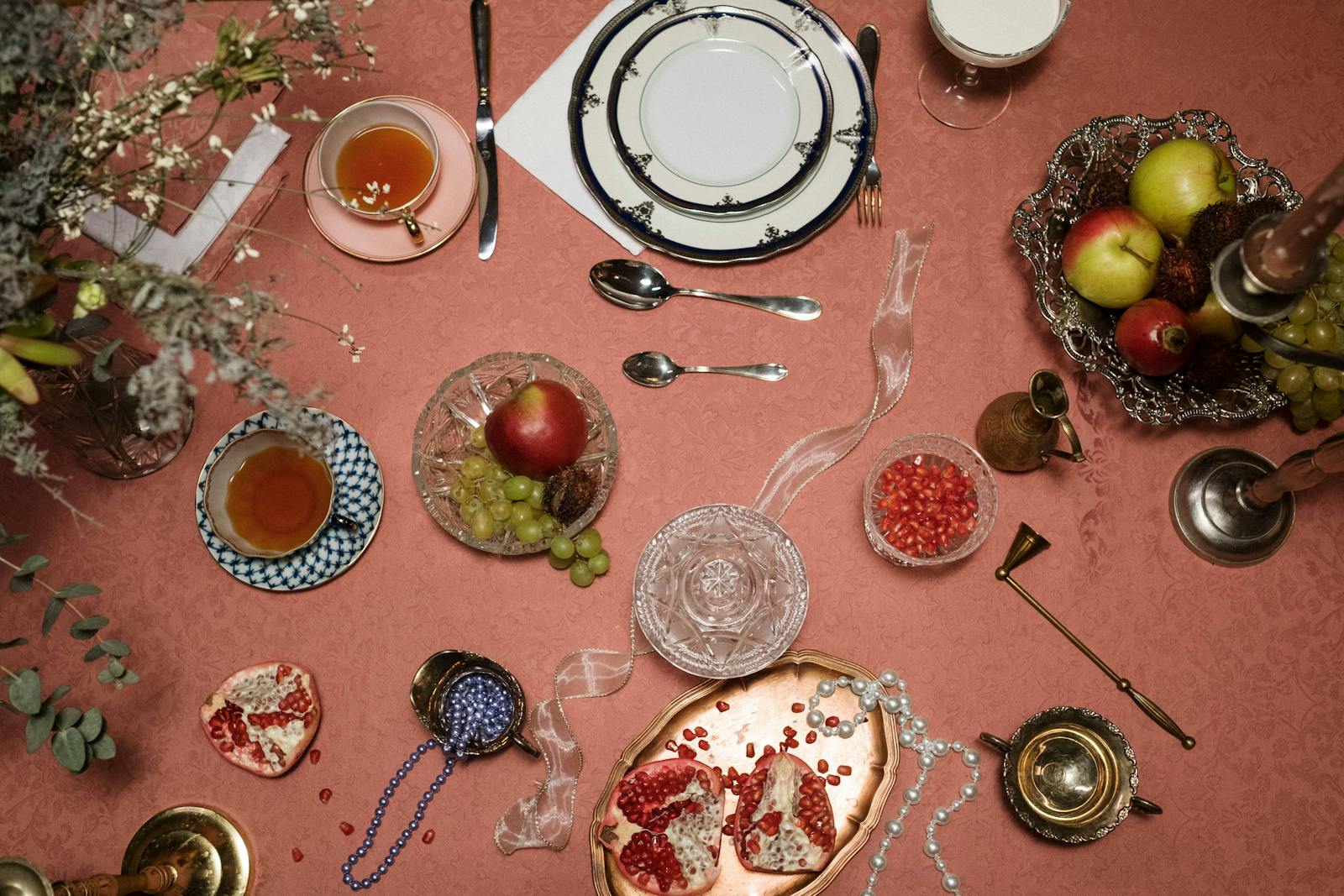 A sophisticated dining setup featuring fresh fruits, tea, and decorative tableware on a pink tablecloth.
