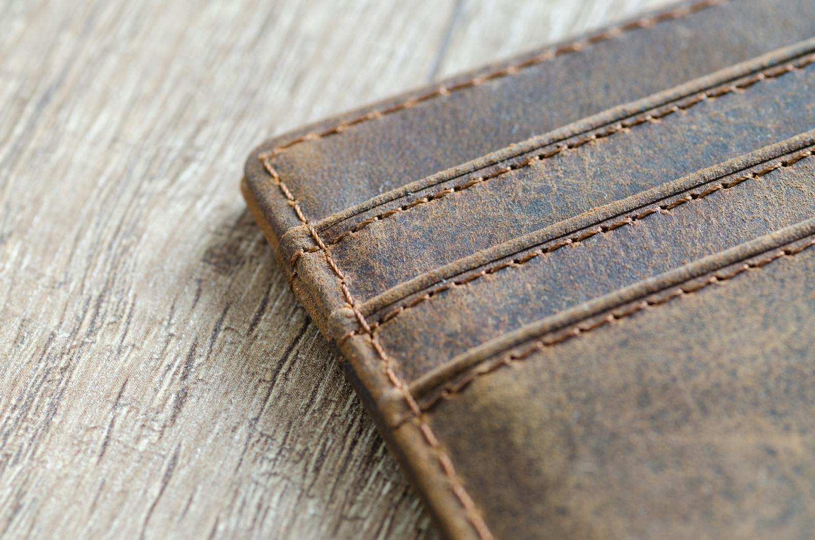 Detailed shot of a brown leather wallet on a textured wooden surface, showcasing stitching.