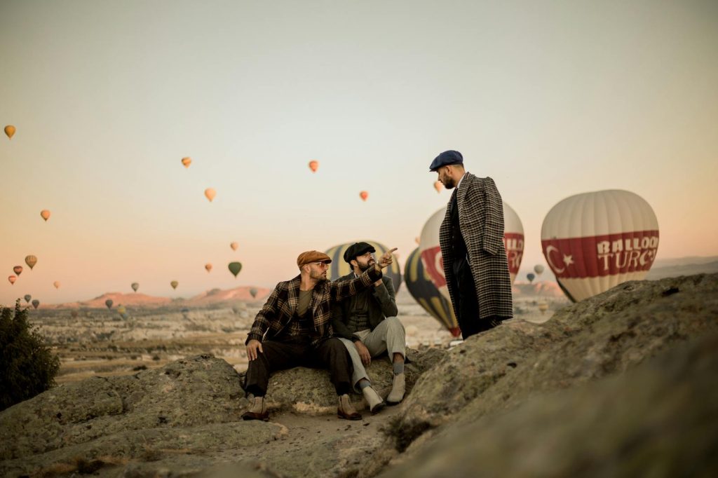 Stylishly dressed men amidst hot air balloons in Cappadocia at sunrise, creating a vintage atmosphere.