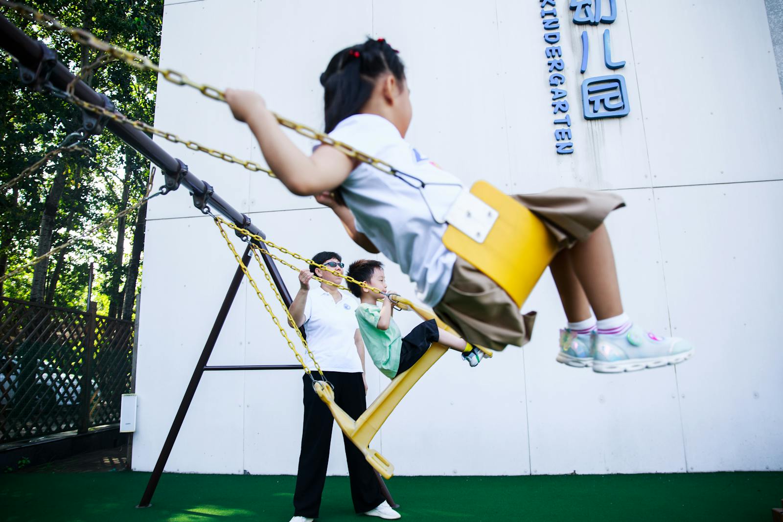 Children enjoying swings in a kindergarten playground on a sunny day.