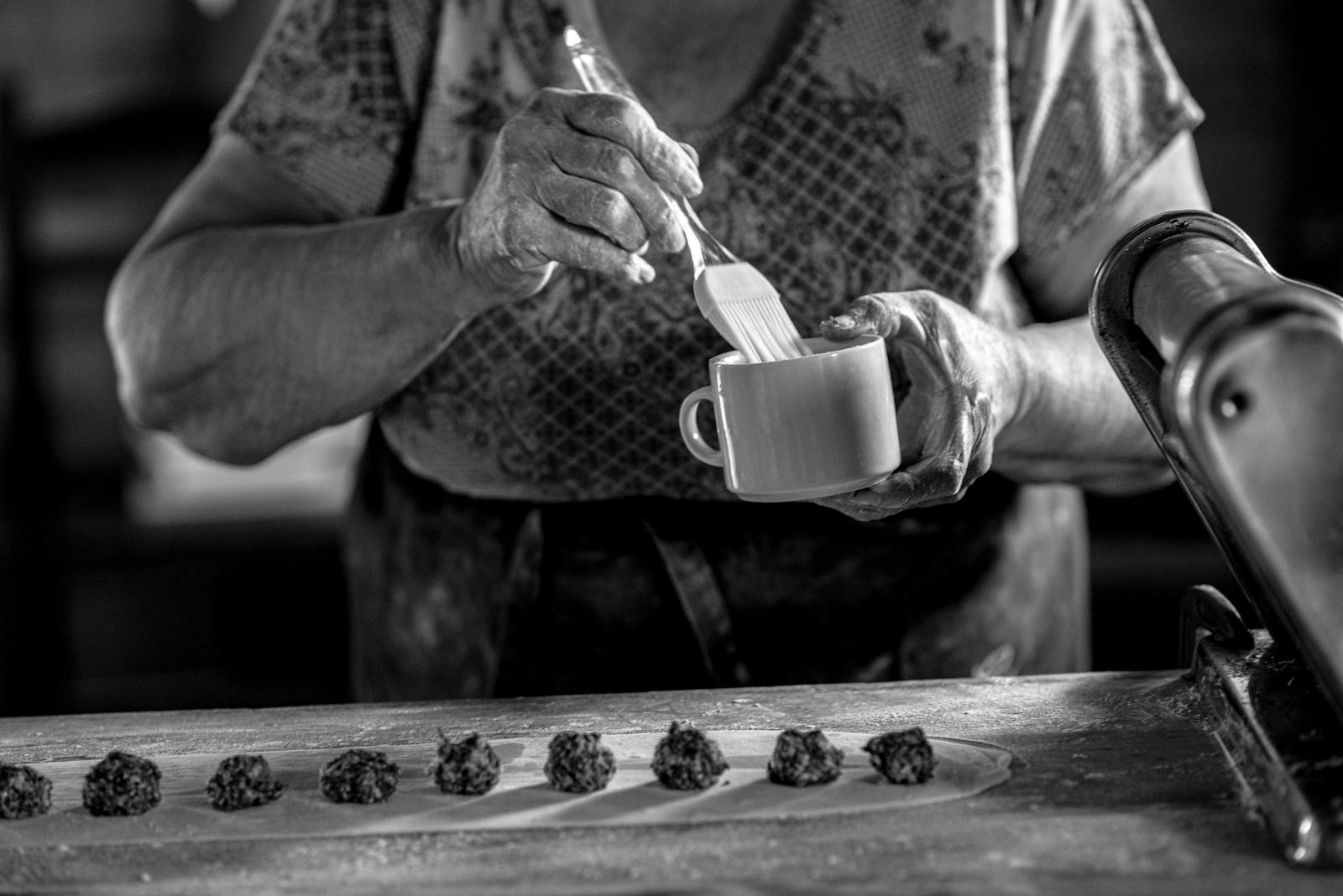 A senior woman prepares homemade pastry in a rustic kitchen setting.