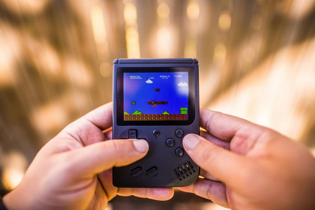 A close-up of hands holding a retro game console playing a classic Mario game outdoors.