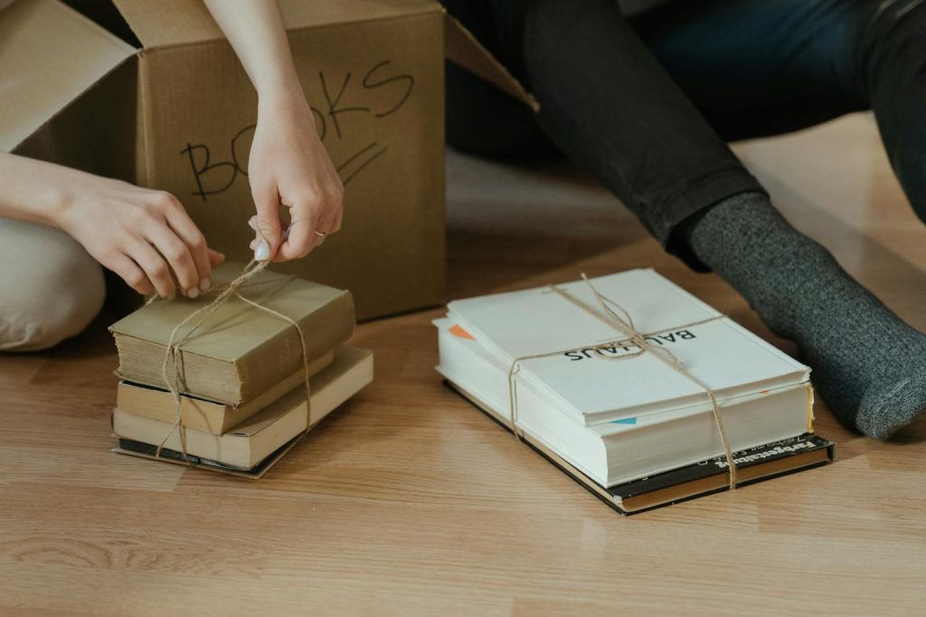 Hands organizing books on the floor next to cardboard box. Ideal for themes of moving and home organization.