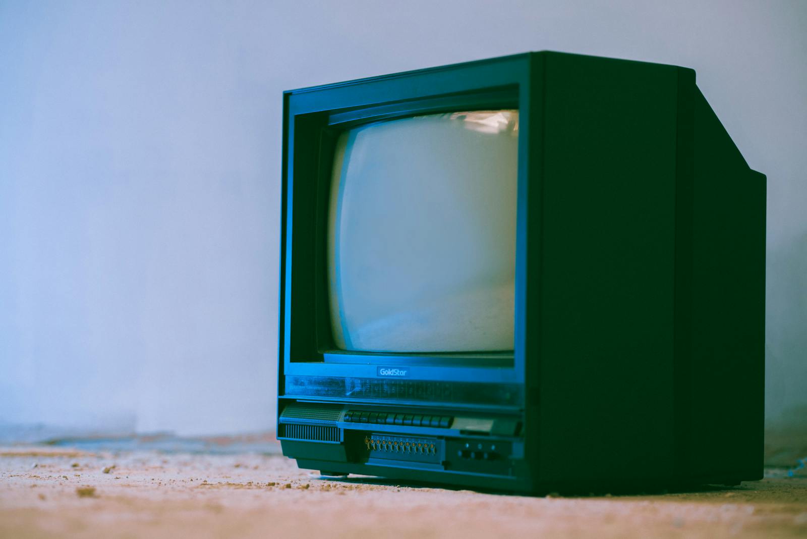 Aged television set with control panel and plastic case near wall in building on white background