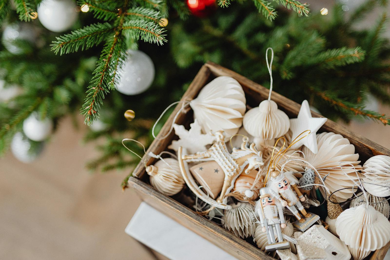 Top view of festive Christmas decorations in a wooden box beside a Christmas tree.
