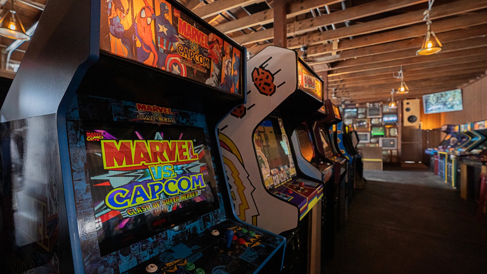 A row of vintage arcade machines in a retro-styled gaming room with dim lighting.