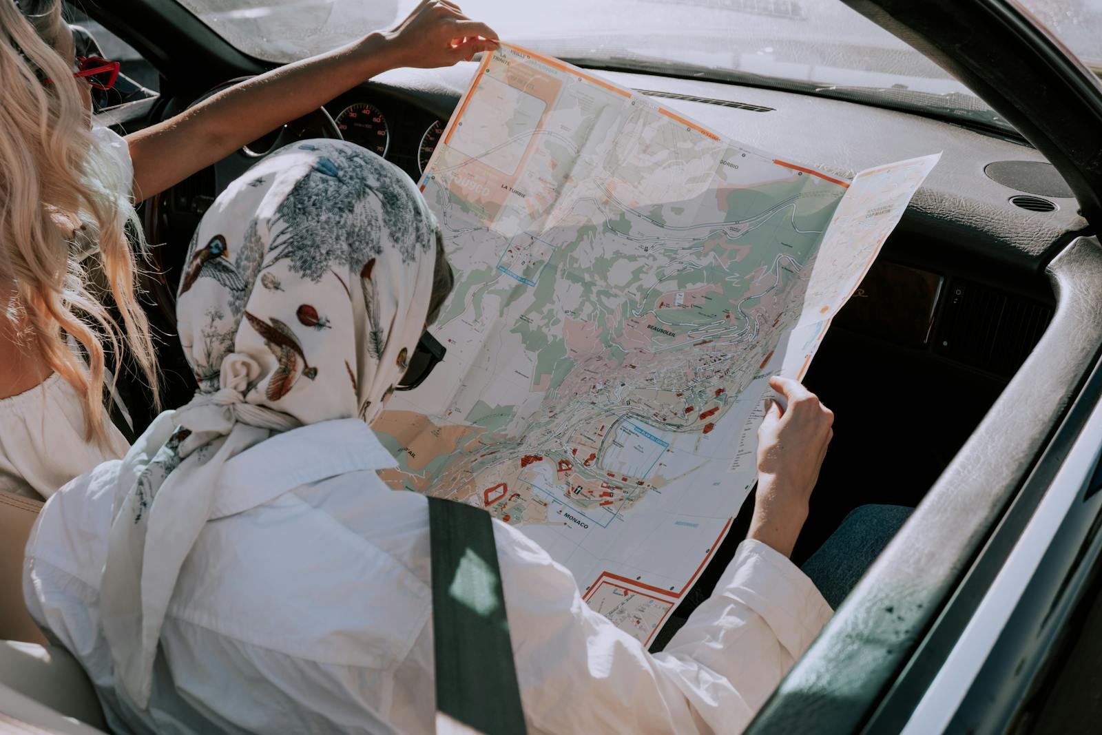 Two friends in a car navigating their road trip using a map during daytime.